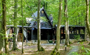 Eine Blockhütte mit steilem Dach und Stein Fundament, umgeben von einem Wald.
