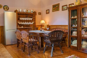 A dining area with a wooden table, chairs, a refrigerator, a cabinet with dishes, and wall decorations. - Authentic Slavonian home with pool, barbecue and orchard (Lug)