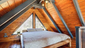 Ein Holzinnenraum mit einem Bett, einem Fenster und einer Decke mit Holzbalken.