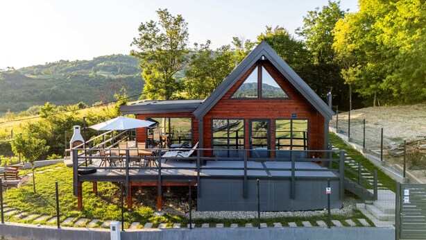 Eine moderne Holz-Blockhütte mit einer Terrasse, großen Fenstern und Blick auf die umliegende Landschaft.