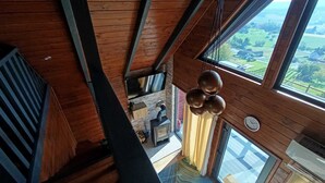 Ein Zimmer mit hohen Decken, einem großen Fenster, einer Hängelampe und einer sichtbaren Uhr.