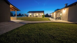 Ein modernes Haus mit gepflegtem Rasen, einer Terrasse und einem überdachten Sitzbereich im Freien.