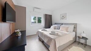 Ein modernes Schlafzimmer mit einem Bett, einem Flachbildfernseher, einem Fenster und einem kleinen Tisch mit einer Lampe.