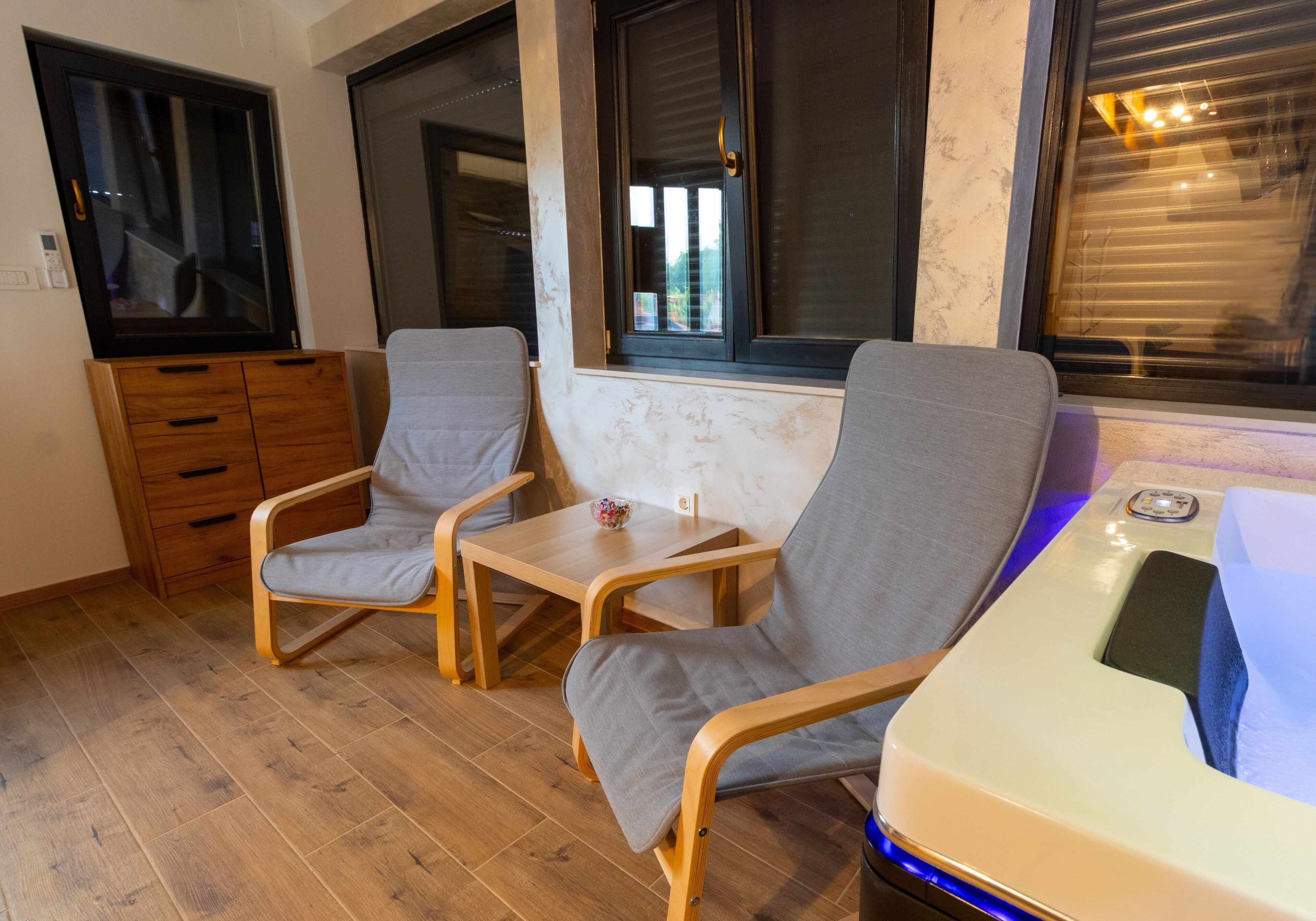 A room with two grey chairs, a wooden table, a wooden cabinet, and a white sink with blue lighting.