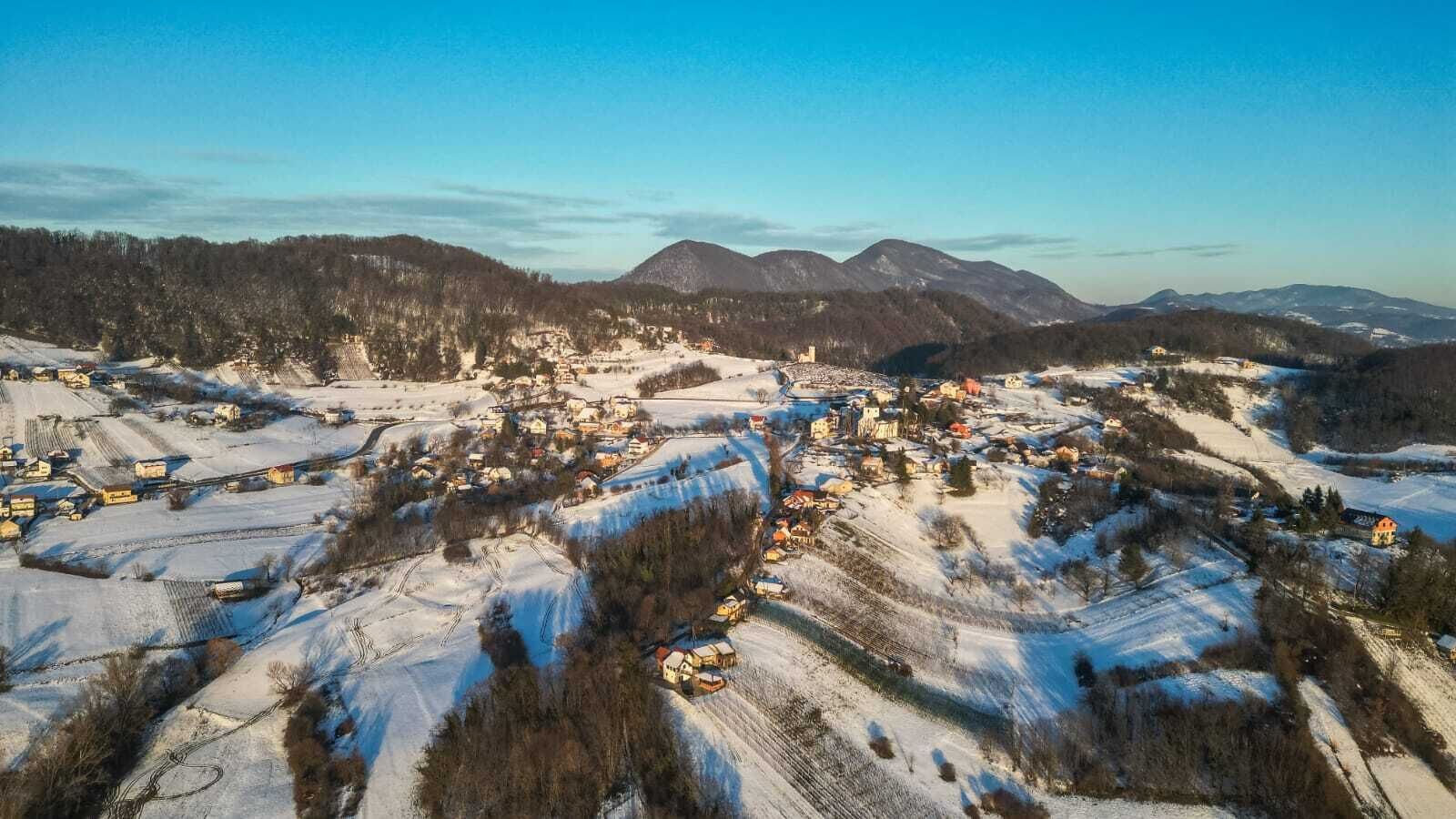 A snow-covered village with houses and fields, surrounded by mountains.