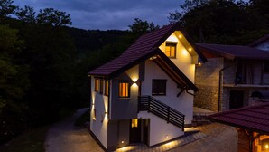 Una casa de dos pisos con techo rojo, un balcón y cimientos de piedra.