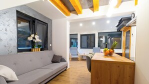 Una sala de estar moderna con un sofá gris, suelo de madera, una mesa de madera con fruta y una ventana con vidrio esmerilado.