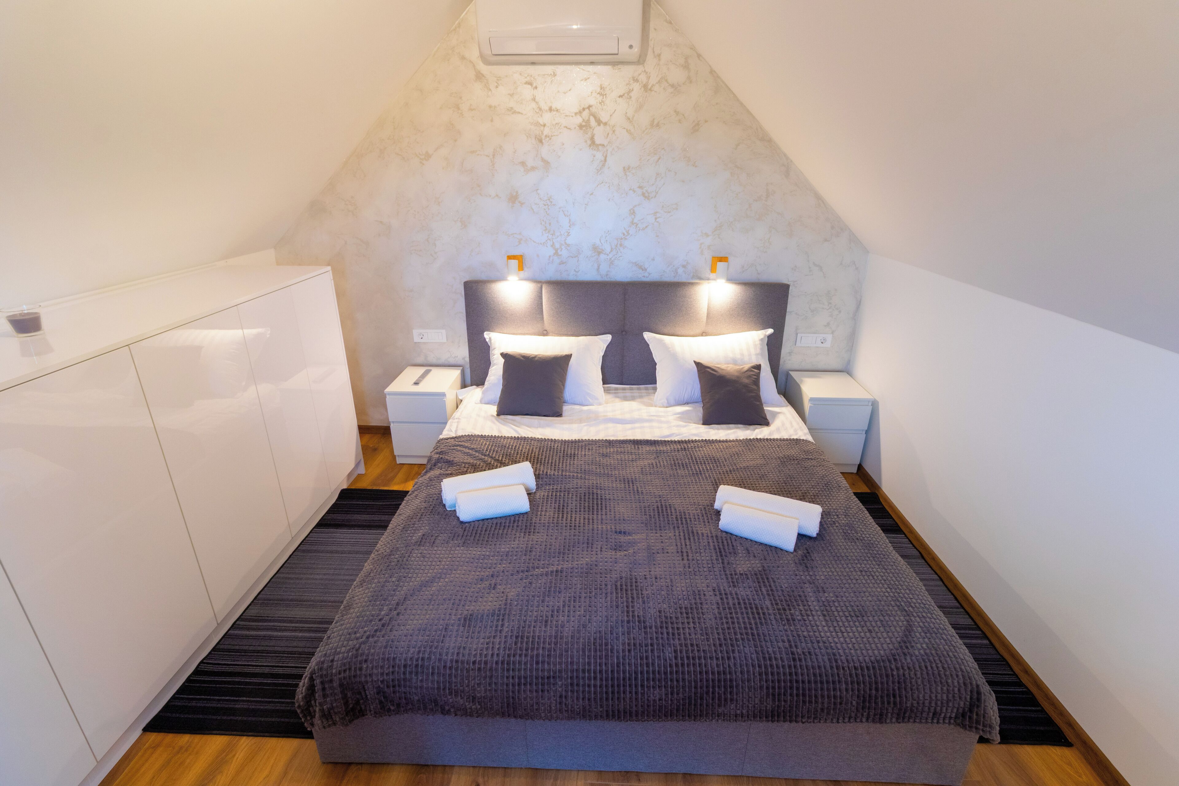 Ein Schlafzimmer mit Bett, Nachttischen, einem Kleiderschrank und einer geneigten Decke.