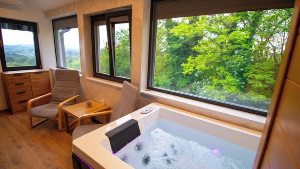 Una habitación con bañera de hidromasaje, muebles de madera y grandes ventanales con vistas a la vegetación.