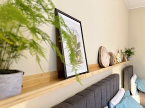 Una stanza con uno scaffale di legno che contiene un quadro incorniciato, una pianta in vaso e oggetti decorativi.