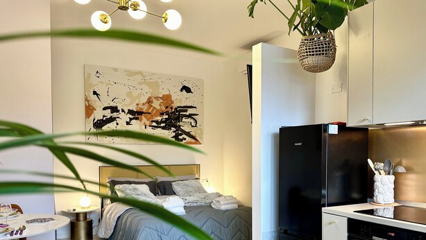A modern bedroom with a bed, a black refrigerator, a kitchen area with a dishwasher, and a large abstract painting on the wall. - Elegant and Private, close to the city center. Gran Dimora dei Sensi e Charme. (Bergamo)