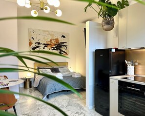 Un dormitorio moderno con una cama, un refrigerador negro, una zona de cocina con lavavajillas y un cuadro abstracto grande en la pared.