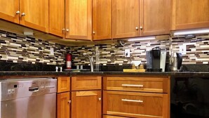 A kitchen with wooden cabinets, a dishwasher, a coffee maker, and a tiled backsplash. - Family friendly neighborhood spacious 3-bedrooms, 2 baths,  parking, near train. (Brookline)