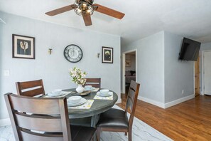 Ein Essbereich mit rundem Tisch, Stühlen, Deckenventilator, Wanduhren und gerahmten Bildern.