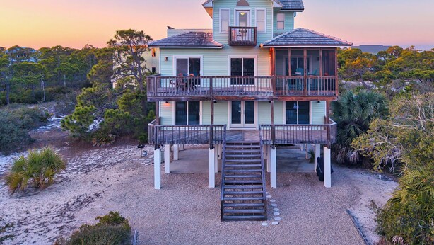 Una casa frente al mar de dos pisos, con un balcón, un porche cubierto y una escalera que lleva a la entrada.