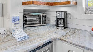 Una cocina con armarios blancos, estantes de madera, horno empotrado, cafetera y lavavajillas.