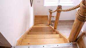 Una escalera de madera con barandilla de metal, una ventana con persianas y una pequeña puerta de madera.
