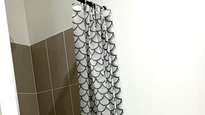 Ducha con cortina estampada, paredes azulejadas y desagüe visible.