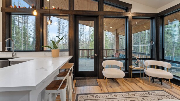 Una cocina moderna con una isla grande, suelo de madera y ventanas amplias que dan a un bosque.