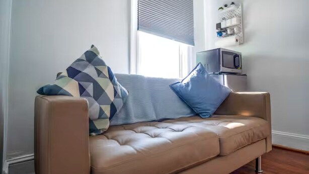 Ein beiges Sofa mit einem gemusterten Kissen, einem blauen Kissen und einem kleinen Tisch mit einem Fernseher.