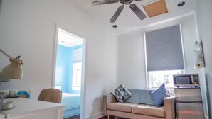 Ein kleiner Wohnbereich mit Küchenzeile, Deckenventilator, einem Bett und einem Fenster mit Jalousien.