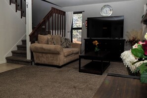 A living room with a sofa, coffee table, TV, staircase, and a clock on the wall.