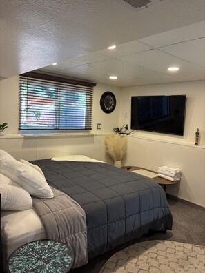 Quarto com cama, televisão, relógio e janela com persianas.