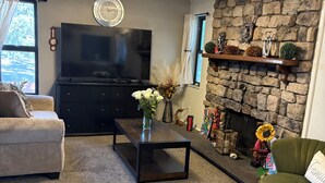 Una sala de estar con chimenea de piedra, un televisor de pantalla plana, un sofá, una mesa de centro y un jarrón decorativo.