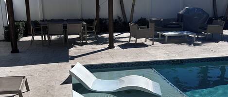 Una piscina con dos toboganes, una parrilla cubierta, mobiliario exterior y una pérgola.