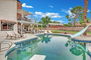 Une piscine avec un toboggan, des chaises longues et un espace patio couvert.