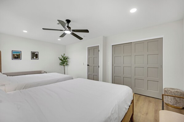 A hotel room with two beds, a ceiling fan, a door, and a small plant. - Vegas Casita Estate | Pool + Private Casita (Las Vegas)