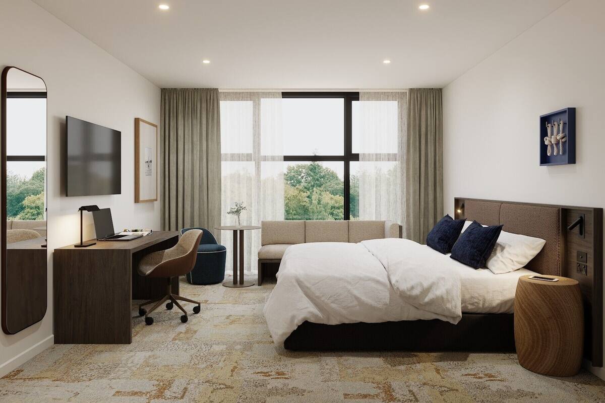 Une chambre d’hôtel équipée d’un lit, d’un bureau, d’une chaise, d’une télévision et de grandes fenêtres.