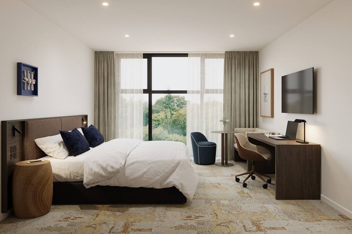Une chambre d’hôtel avec un lit, un bureau, une chaise et un téléviseur fixé au mur.
