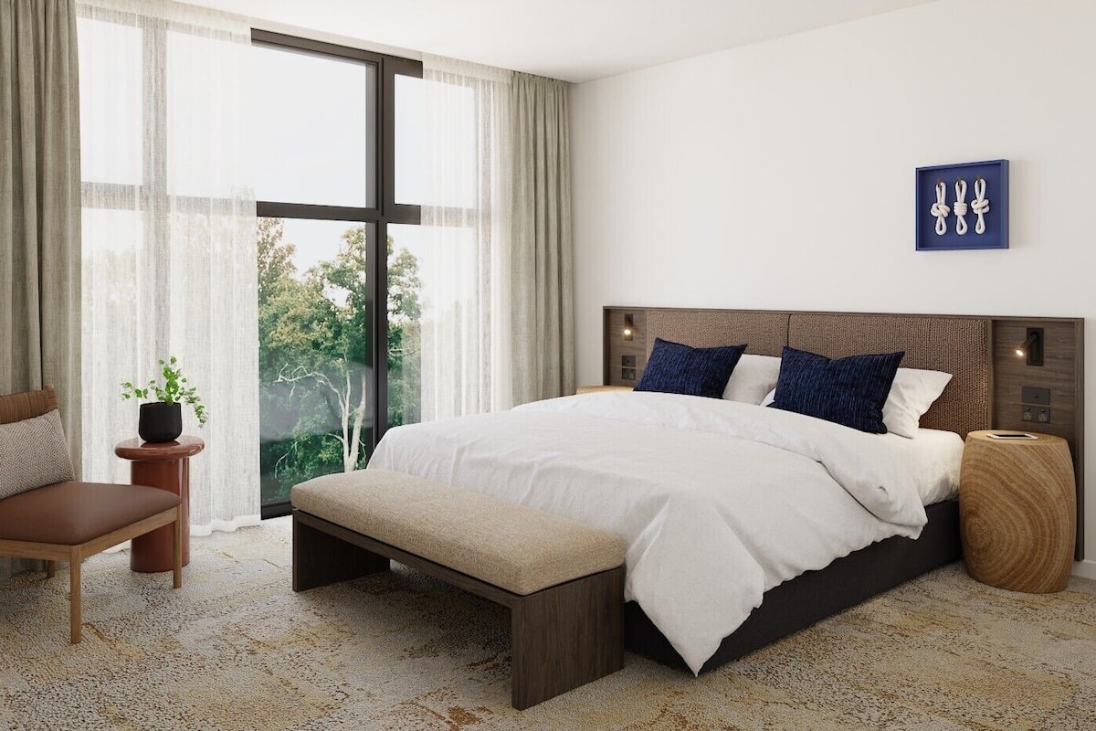Une chambre moderne avec un grand lit, une chaise, une table de chevet et une vue sur la verdure.
