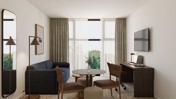 Ein modernes Hotelzimmer mit einer Sitzecke, einem runden Tisch, Stühlen, einem Schreibtisch, einem Fernseher und einem großen Fenster mit Vorhängen.