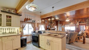 Een keuken met een centraal eiland, een eethoek met een houten tafel en een open haard versierd met geweivleugels.