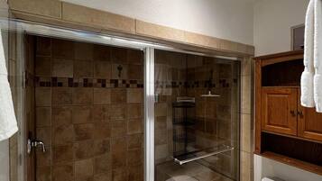 A bathroom with a glass-enclosed shower, a toilet, and a wooden cabinet.