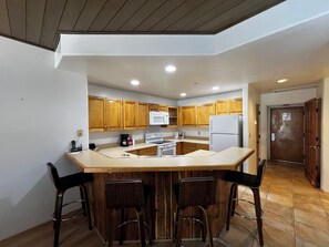 A kitchen with wooden cabinets, a white refrigerator, a stove, and a bar area with stools. - Enjoy stunning mountain views at Eolus 428, a cozy 2-bedroom condo in Purgatory Village. (Durango)