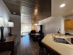 A kitchen with wooden cabinets, a sink, and a dining area with a table and chairs. - Enjoy stunning mountain views at Eolus 428, a cozy 2-bedroom condo in Purgatory Village. (Durango)