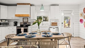 Een keuken met witte kasten, een houten plafond, een eettafel met stoelen en een vaas met een plant.