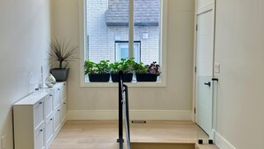 Un escalier menant à un palier avec une fenêtre, une armoire blanche et des plantes en pot.