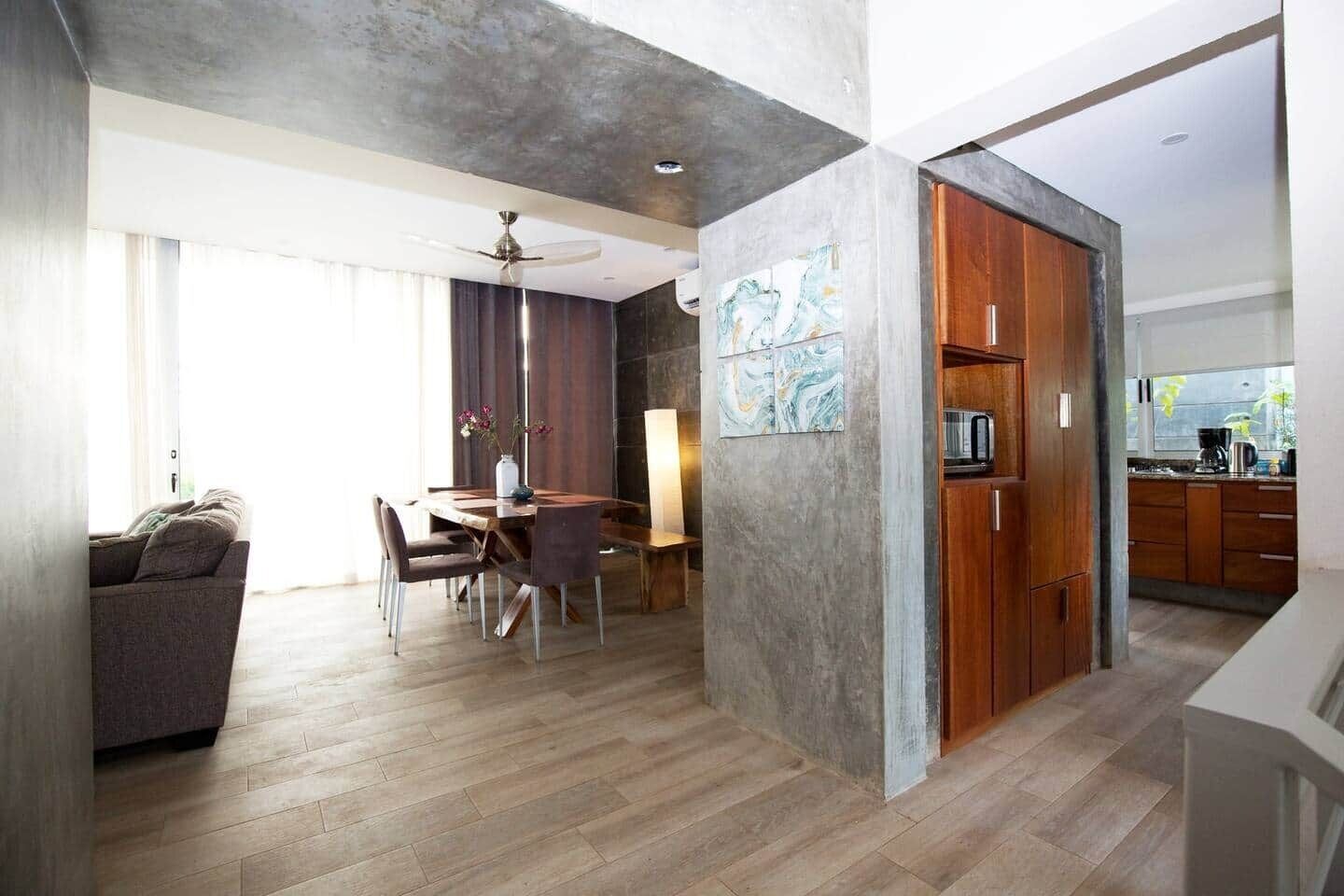 A modern living space with a dining area, kitchen, and a large window providing natural light.