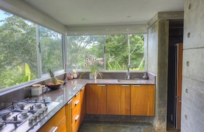 Een keuken met een gasfornuis, houten kastjes, een spoelbak en een raam met uitzicht op groen.