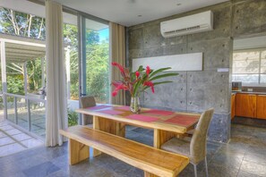 Un comedor moderno con una mesa de madera, un banco y una silla, un jarrón con flores y vistas a zonas verdes.
