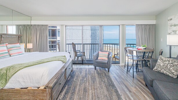 Habitación de hotel con cama, balcón con mesa y sillas, y vista al mar.