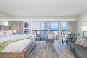 Ett hotellrum med en säng, en balkong med ett bord och stolar samt utsikt över havet.