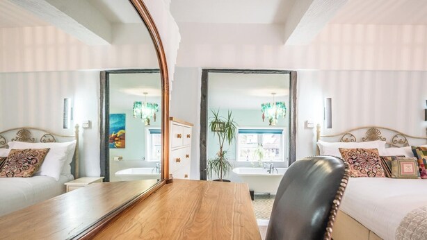 Una camera d'albergo con un tavolo di legno, due letti, uno specchio grande e vista sul bagno.