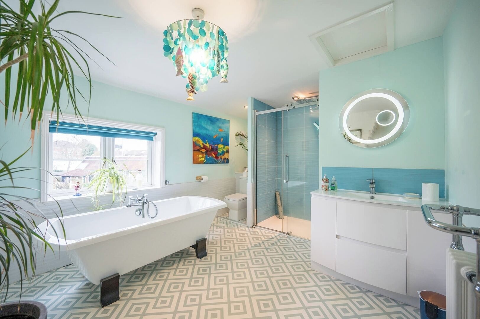 A bathroom with a freestanding bathtub, a glass shower enclosure, a round mirror, and a patterned floor.