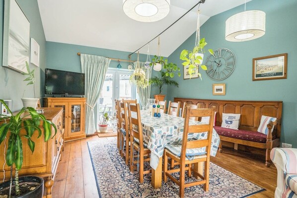 A dining area with a table set for six, surrounded by wooden chairs, a wooden bench, and a television on the left. - The Old Bakery, Wrentham (Wrentham)
