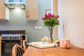 A kitchen with a stove, a vase with flowers, a cake, and a notebook on the table. - 40 Grimsey Road, Leiston (Suffolk)